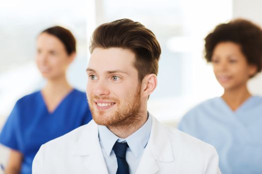 clinic, profession, people and medicine concept - happy male doctor over group of medics meeting at hospital