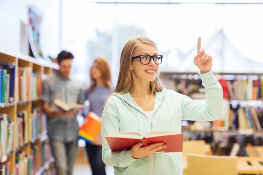 people, knowledge, education and school concept - happy student girl or young woman with book in library