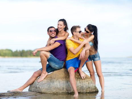 friendship, sea, summer holidays, beach and people concept - group of happy friends sitting on rock