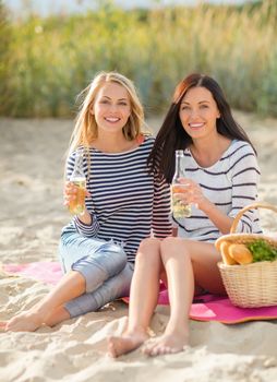 summer holidays, vacation, celebration and people concept - happy teenage girls or young women having picnic and drinking beer or lemonade on beach