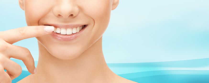 dental health, beauty, hygiene and people concept - close up of smiling woman face pointing to teeth over blue wavy background