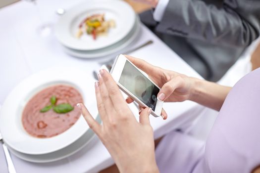 people, leisure, eating and technology concept - close up of couple with smartphones taking picture of food at restaurant