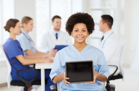 clinic, profession, people and medicine concept - happy female doctor or nurse showing tablet pc computer blank screen over group of medics meeting at hospital