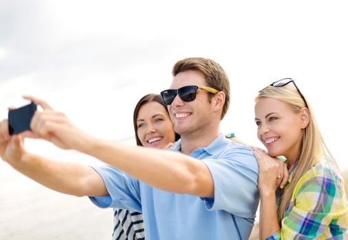 summer holidays, vacation, happy people concept - group of friends taking selfie with cell phone on the beach