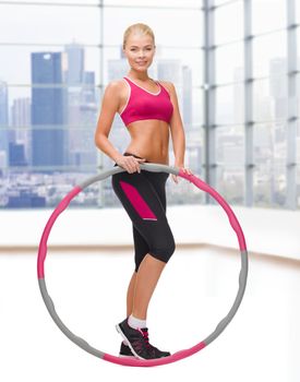 fitness, sport, people and healthcare concept - young sporty woman exercising with hula hoop over gym background