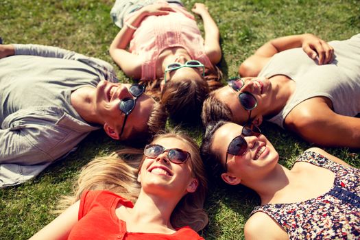 friendship, leisure, summer and people concept - group of smiling friends lying on grass in circle outdoors