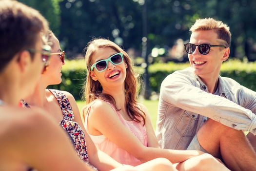 friendship, leisure, summer and people concept - group of smiling friends outdoors sitting on grass in park