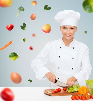 cooking and food concept - smiling female chef, cook or baker chopping vegetables over gray background