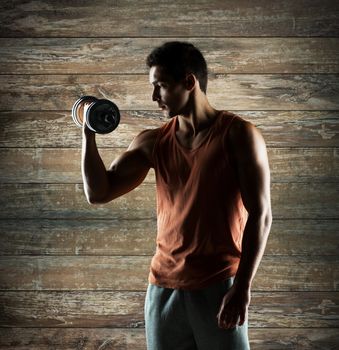 sport, fitness, weightlifting, bodybuilding and people concept - young man with dumbbell flexing biceps over wooden wall background
