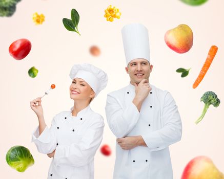 cooking, profession, inspiration, vegetarian diet and people concept - happy chef couple or cooks eating and thinking over beige background with falling vegetables