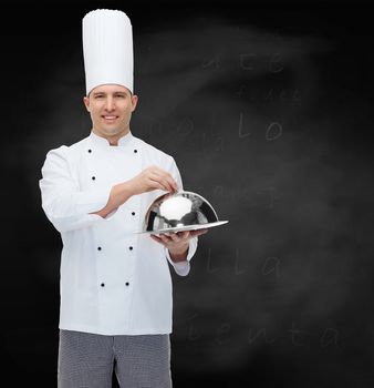 cooking, profession and people concept - happy male chef cook holding cloche over black chalk board background