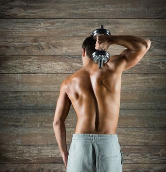 sport, fitness, weightlifting, bodybuilding and people concept - young man with dumbbell flexing biceps over wooden wall background from back