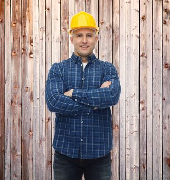 repair, construction, building, people and maintenance concept - smiling male builder or manual worker in helmet over wooden fence background