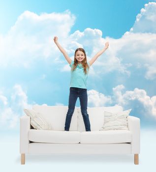 home, leisure, people and happiness concept - smiling little girl jumping on sofa over blue sky and white clouds background