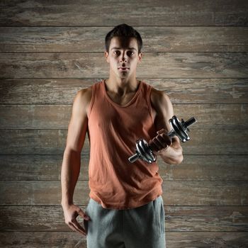 sport, fitness, weightlifting, bodybuilding and people concept - young man with dumbbell flexing biceps over wooden wall background