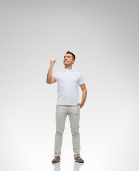 happiness, gesture and people concept - smiling man pointing finger up over gray background