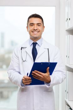 medicine, profession, technology and people concept - happy male doctor with clipboard in medical office