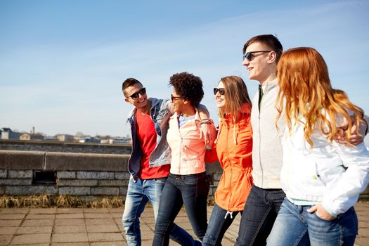 tourism, travel, people and leisure concept - group of happy teenage friends walking along city street and talking