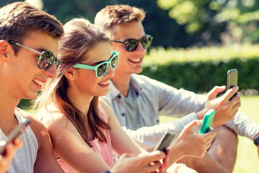 friendship, leisure, summer, technology and people concept - group of smiling friends with smartphones sitting on grass in park