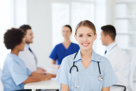 clinic, profession, people and medicine concept - happy female doctor over group of medics meeting at hospital