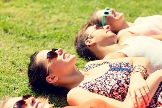 friendship, leisure, summer and people concept - group of smiling friends lying on grass outdoors