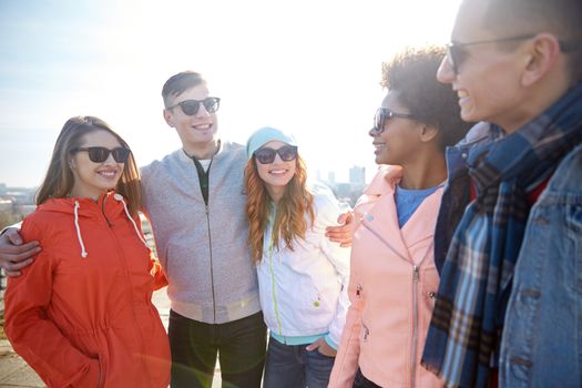 tourism, travel, people, leisure and teenage concept - group of happy friends in sunglasses hugging and talking on city street