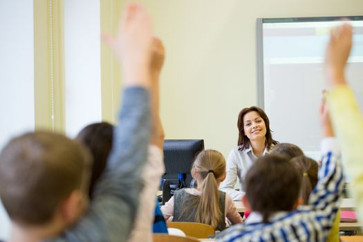 education, elementary school, learning and people concept - group of school kids with teacher sitting in classroom and raising hands