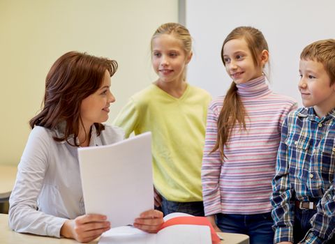 education, elementary school, learning and people concept - group of school kids with teacher talking in classroom