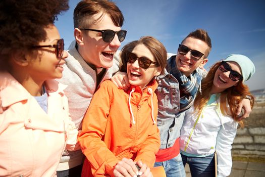 tourism, travel, people, leisure and teenage concept - group of happy friends in sunglasses hugging and laughing on city street