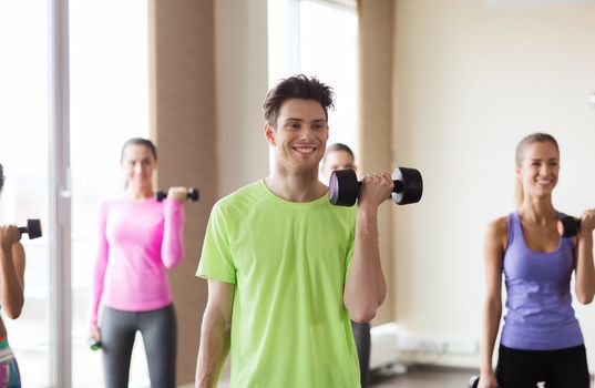 fitness, sport, training, gym and lifestyle concept - group of smiling people working out with dumbbells flexing muscles s in gym