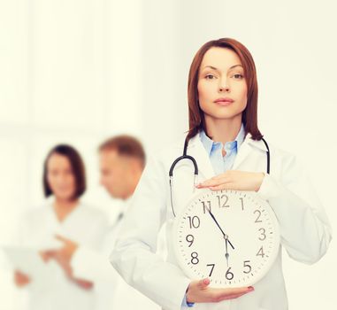 healthcare and medicine concept - calm female doctor with wall clock and stethoscope