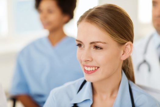 clinic, profession, people and medicine concept - happy female doctor over group of medics meeting at hospital