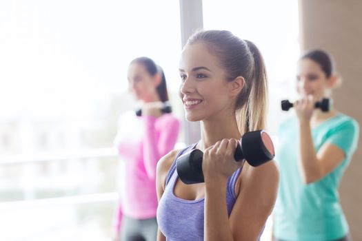 fitness, sport, training and lifestyle concept - group of happy women with dumbbells flexing muscles in gym