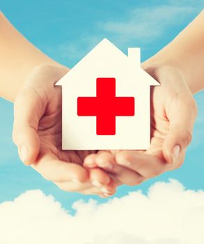 healthcare, medicine and charity concept - hands holding white paper house with red cross sign