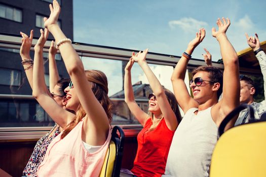 friendship, travel, vacation, summer and people concept - group of smiling friends traveling by tour bus and waving hands