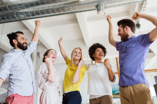 business, triumph, gesture, people and teamwork concept - happy creative team raising hands up and celebrating victory in office