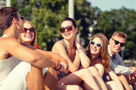 friendship, leisure, summer and people concept - group of smiling friends sitting on city street