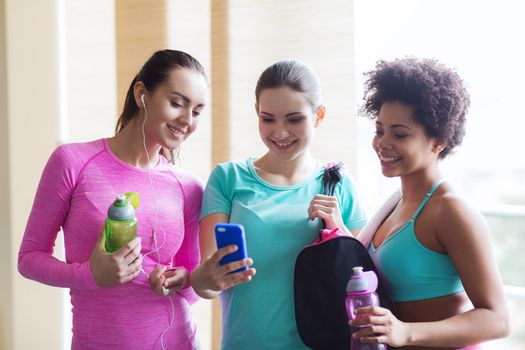 fitness, sport, training, gym and lifestyle concept - group of happy women with bottles and smartphone in gym