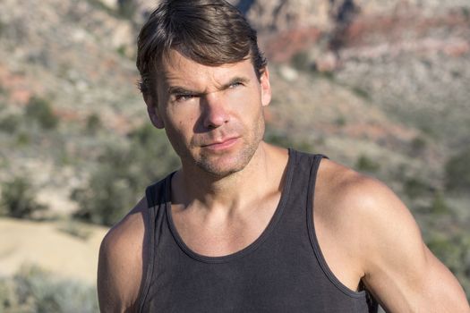 Closeup head shot of bold adventurous Caucasian man with serious expression gazing in bright sunlight in the distant desert