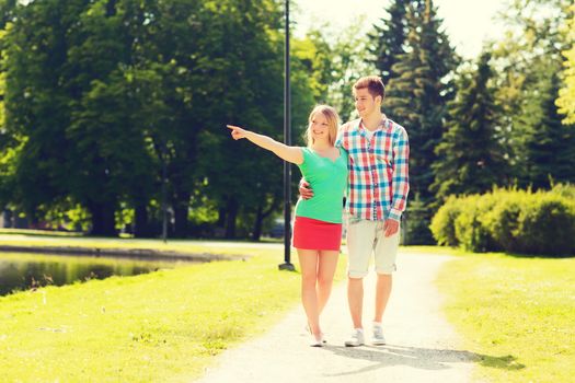 holidays, vacation, love and friendship concept - smiling couple walking and pointing finger in park