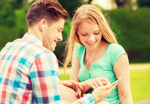 summer, vacation, holidays, technology and friendship concept - smiling couple with smartphone and earphones sitting in park