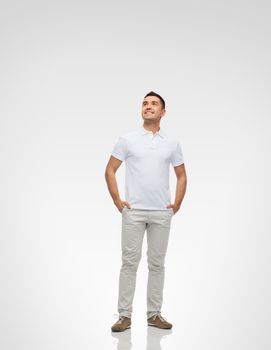 happiness and people concept - smiling man with hands in pockets looking up over gray background