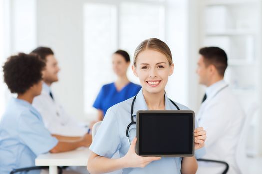 clinic, profession, people and medicine concept - happy female doctor showing tablet pc computer blank screen over group of medics meeting at hospital