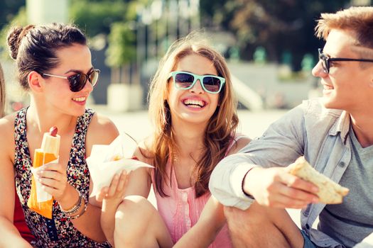 friendship, leisure, summer and people concept - group of smiling friends in sunglasses sitting with food on city square