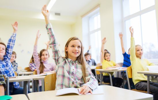 education, elementary school, learning and people concept - group of school kids with notebooks sitting in classroom and raising hands