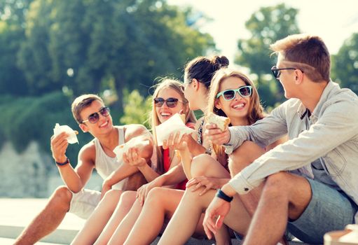 friendship, leisure, summer and people concept - group of smiling friends in sunglasses sitting with food on city square