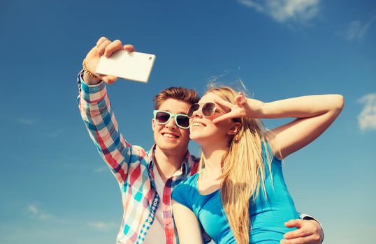 summer, vacation, holidays, technology and friendship concept - smiling couple with smartphone making selfie outdoors