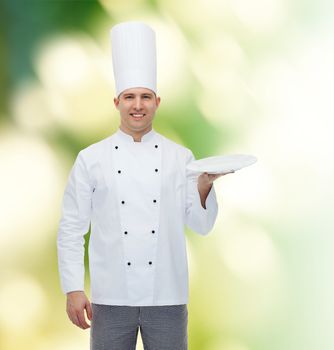 cooking, profession, advertisement and people concept - happy male chef cook showing something on empty plate over green background