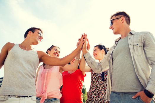 friendship, leisure, summer, gesturer and people concept - group of smiling friends making high five outdoors