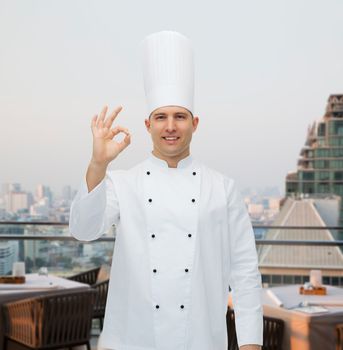 cooking, profession, gesture and people concept - happy male chef cook showing ok sign over city restaurant lounge background